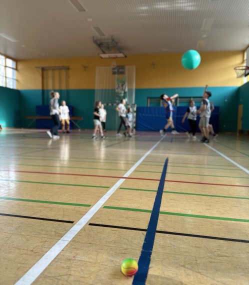 Die Teilnehmenden spielen SustainaBall mit einem großen Gummiball. Im Vordergrund liegt ein kleiner Tennisball.